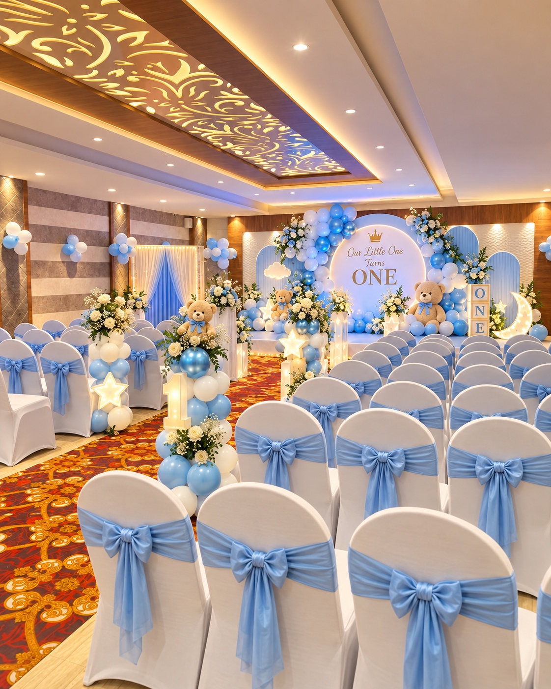Décor concept at Veloria Grand Jayanagar: powder-blue balloons, teddy bears and blue chair sashes around a first-birthday backdrop